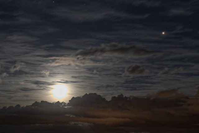 A moonrise behind two layers of cloud