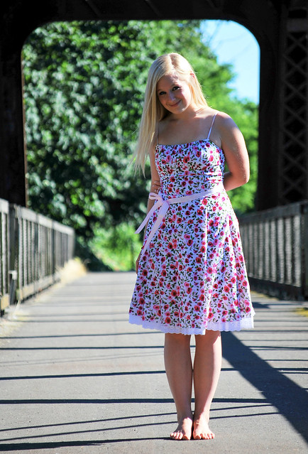 Young woman in flower dress standing barefoot on a bridge