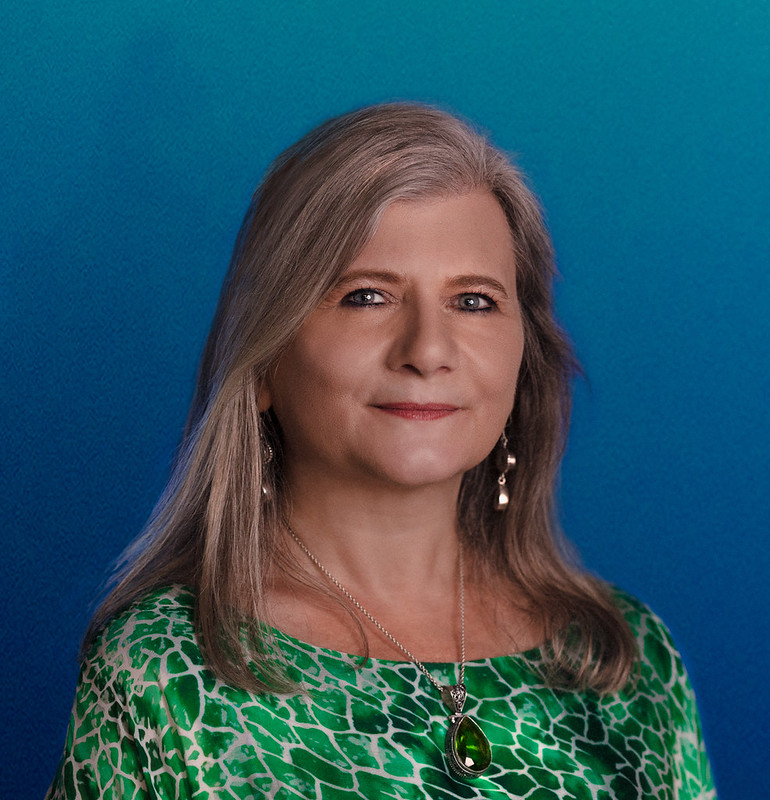 Professor Penny Jane Burke has long grey hair and is wearing an emerald green blouse.
