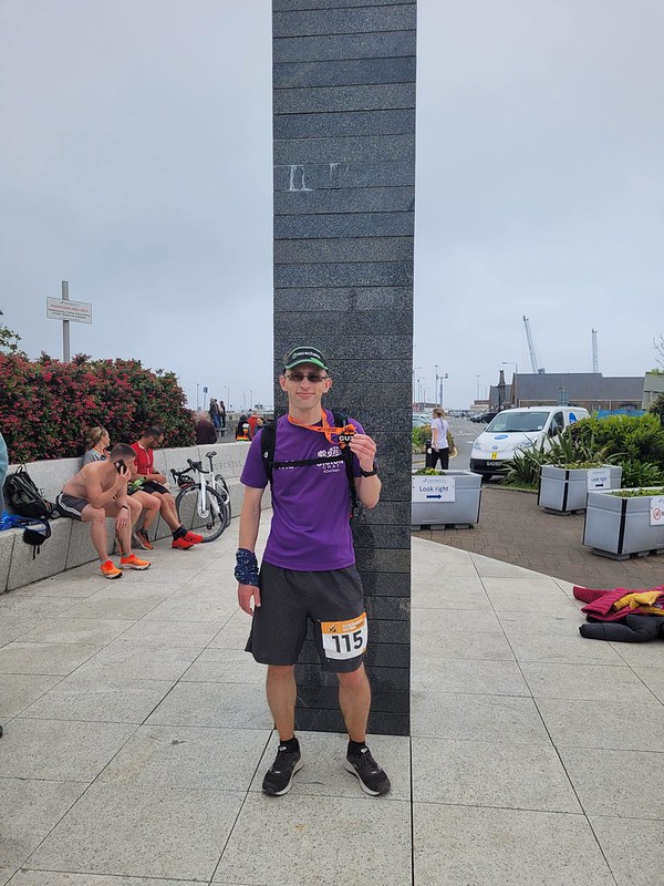 A male runner standing in front of Saint Peter Port's Liberation monument, and holding up a medal