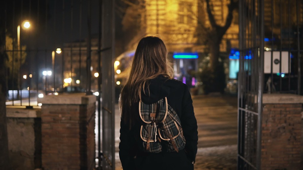 A photo of a young woman walking alone on a street at night