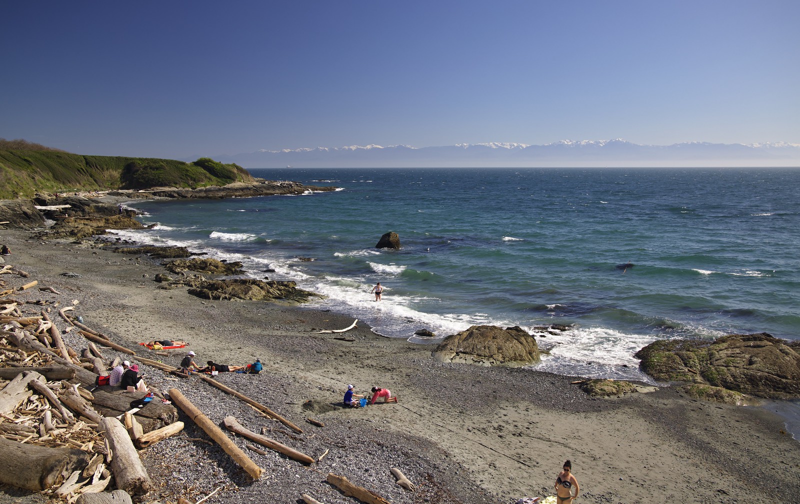 People enjoying the beach with Holland Point and the Olympic Mountains behind
