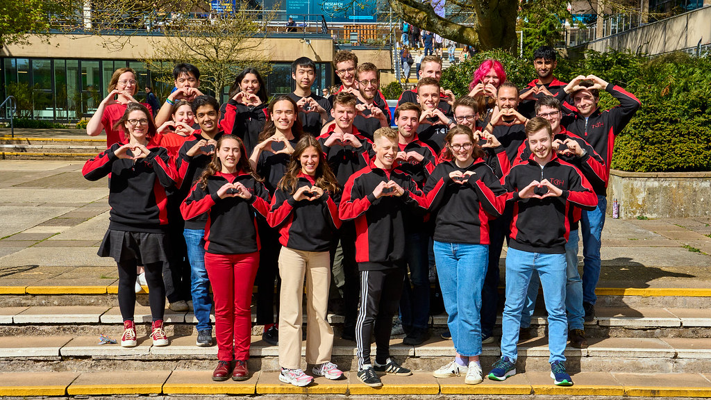 Large group of students stand together facing camera, making heart shape with their hands