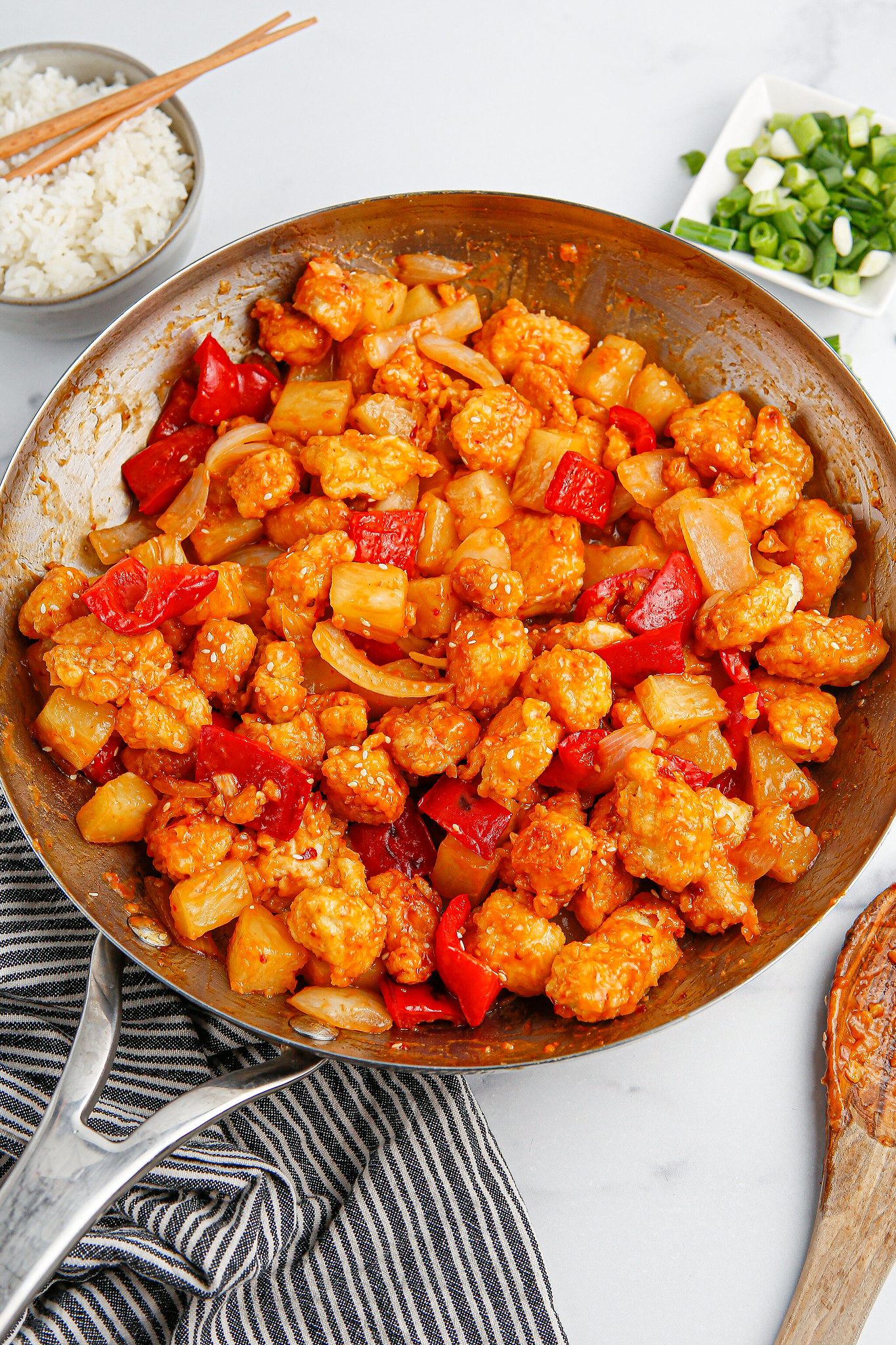 A skillet full of crispy chicken stir fry with onion, red bell pepper, and pineapple