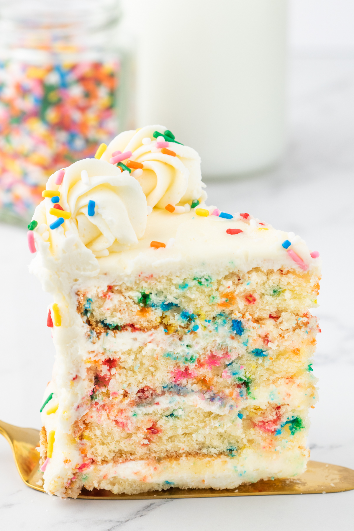 A slice of funfetti cake topped with vanilla buttercream and rainbow sprinkles