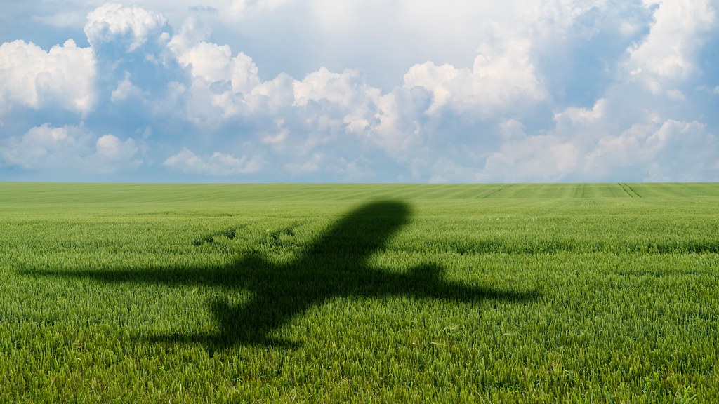 A photo of a shadow of a jet airliner cast on a green field