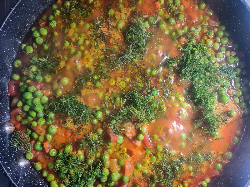 The stew bubbling in the pan, with fresh chopped dill added on top