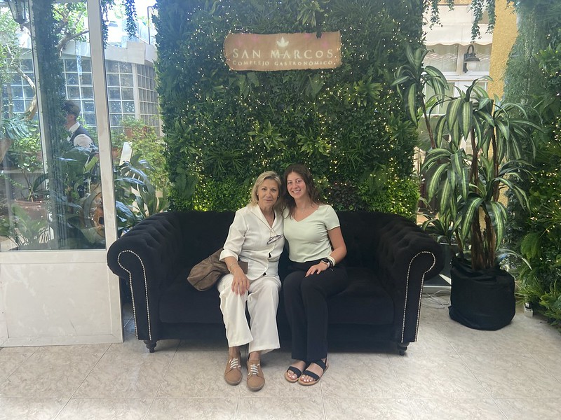 Leslie and her host mom sitting on a couch smiling in front of some greenery at a restaurant