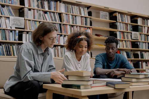 Three people sit at a library table and look at the books that sit in front of them - How to Meet With Your Academic Advisor