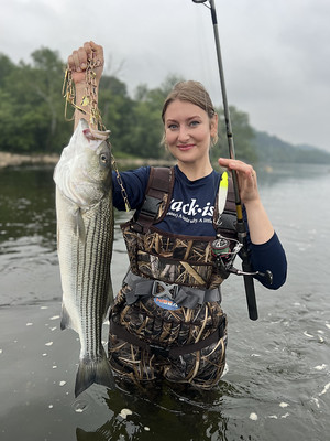Photo of woman in a river holding up a large striped bass