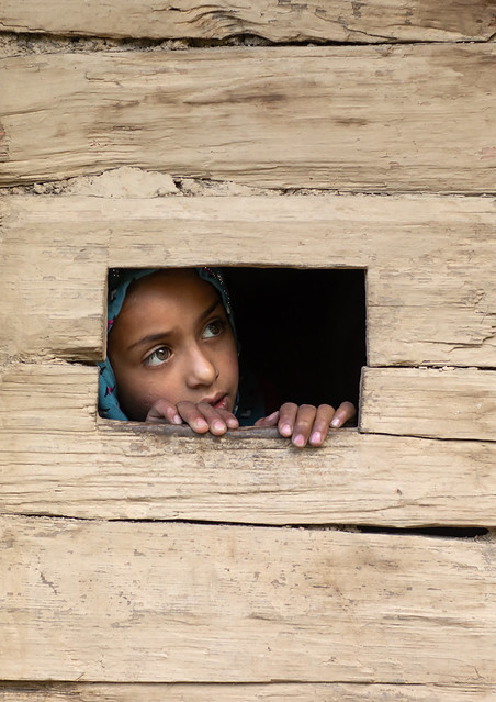 Gujjar Bakerwal girl looking through a hole in a house, Jammu and Kashmir, Kangan, India