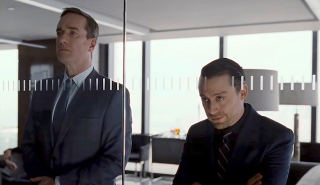 Tom and Roman gaze out through the glass wall of a corporate office