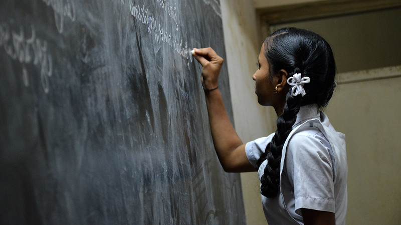 A young girl writing on a chalk board in a school classroom.