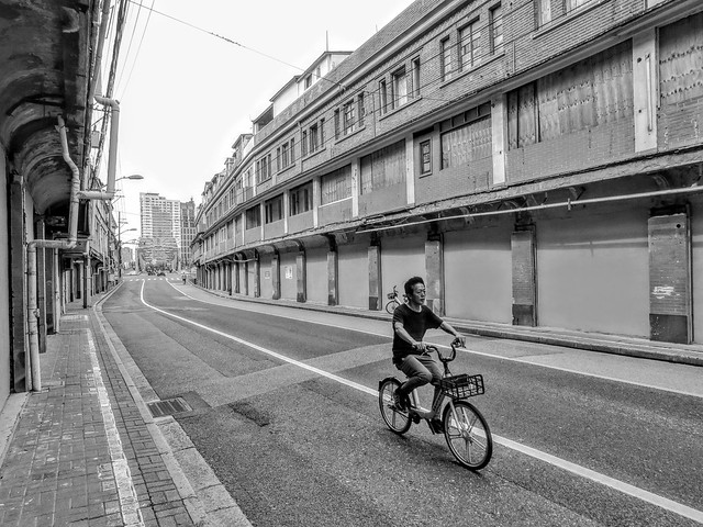 A man cycles through an empty street lined with old buildings that have been sealed off and are about to be demolished.