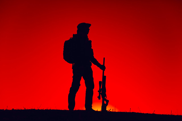 Elite forces sniper patrolling with gun on sunset