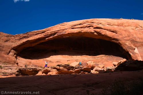 Two hikers standing under Longbow Arch near Moab, Utah