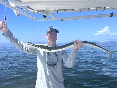 Photo of man on a boat holding a long, thin fish