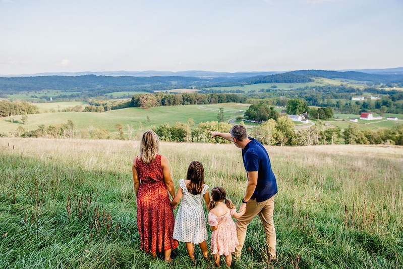 A family viewed from behind, looking at a wide vista of fields and rolling hills.