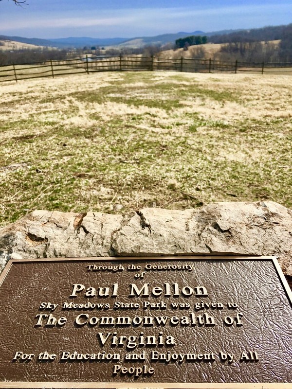 A large metal plaque on a stone in front of a pastoral landscape. Plaque reads: Through the Generosity of Paul Mellon Sky Meadows State Park was given to the Commonwealth of Virginia For the Education and Enjoyment by All People.