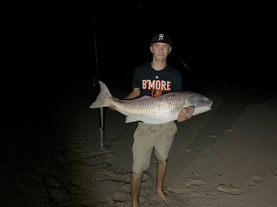 Photo of man holding a fish, on a beach at night