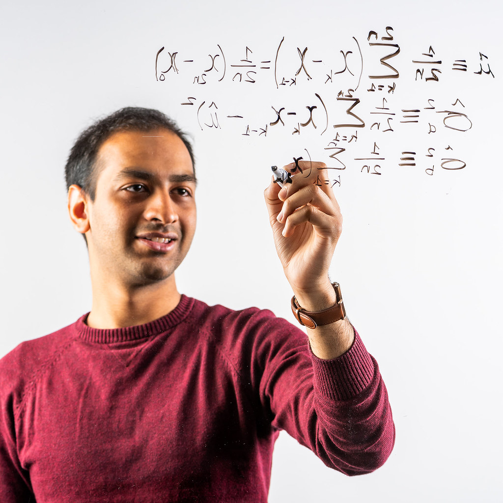 A person writing mathematical equations on a perspex board.