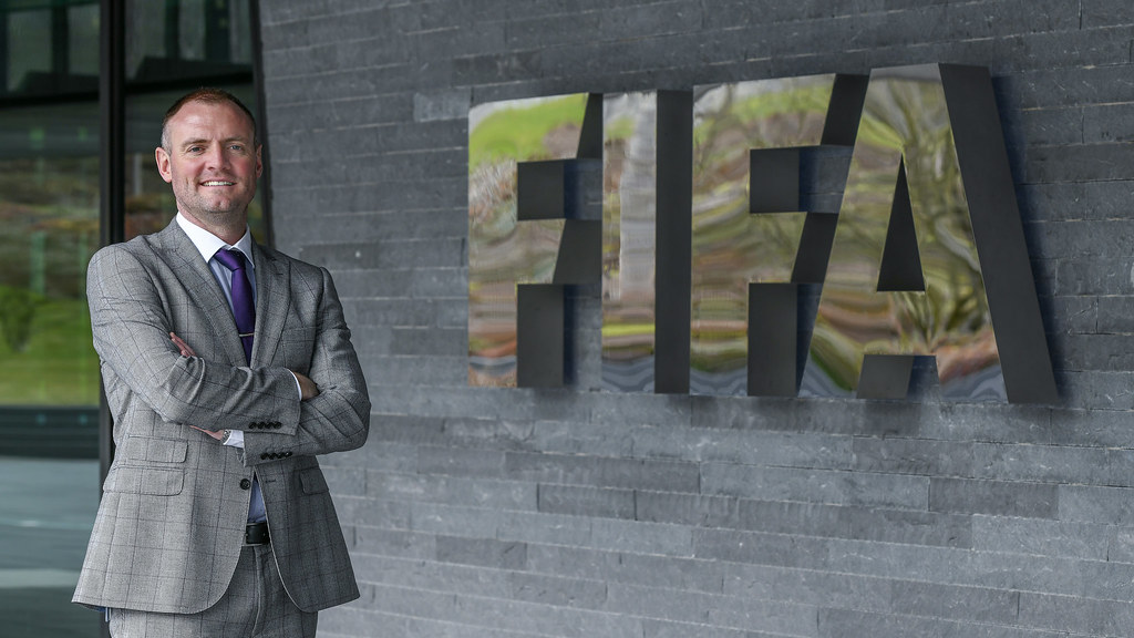 A man (Dr Andrew Massey) stood in front of a FIFA sign.