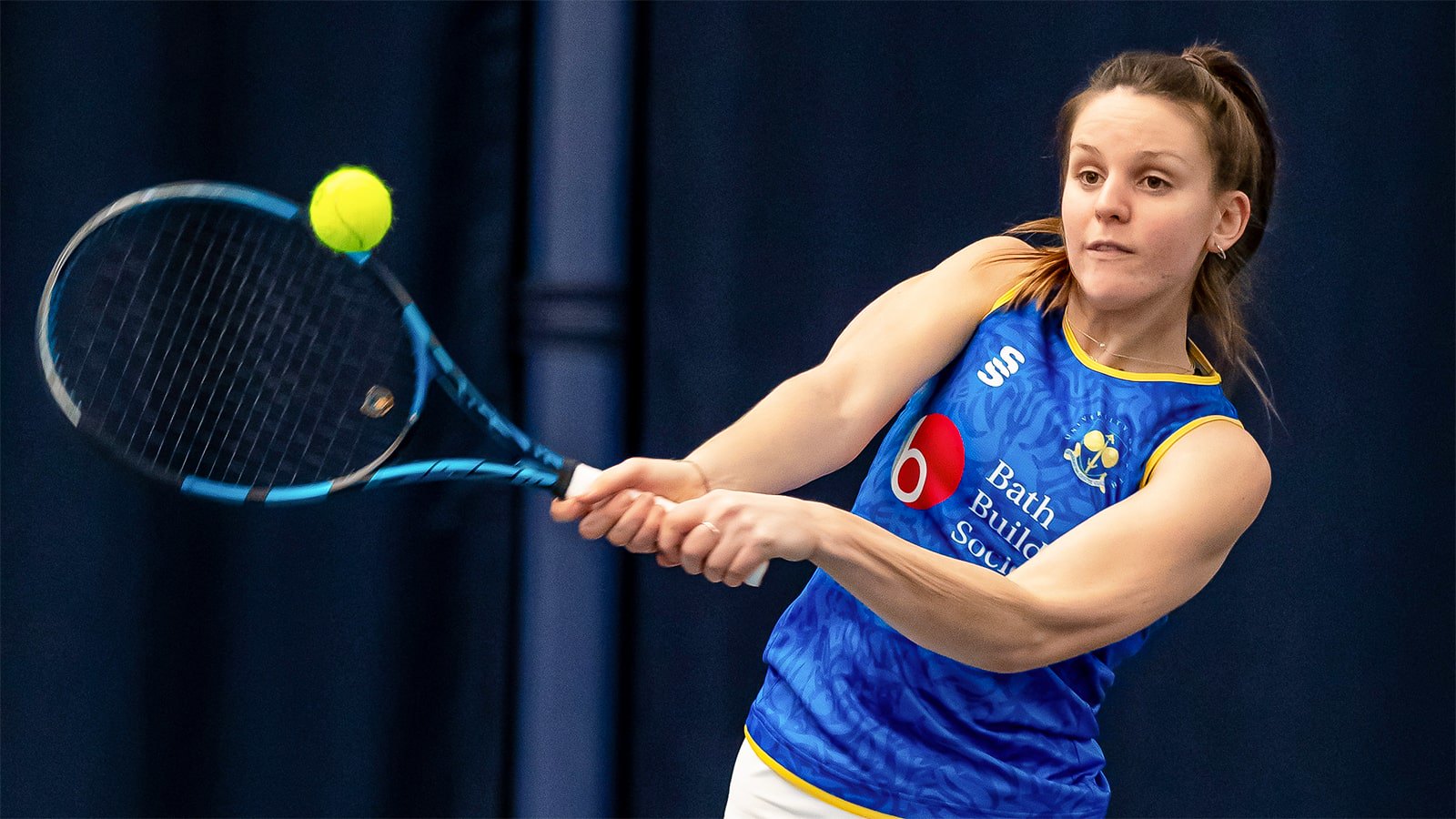 A student hitting a ball with a tennis racket.