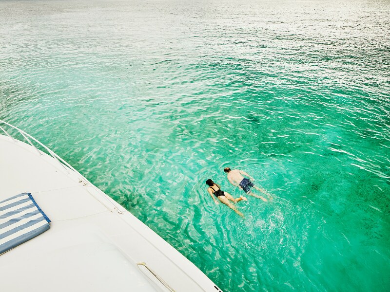Two people black wearing swimsuits, snorkelling on the side of a boat