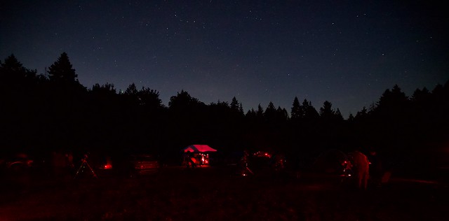 Camping and telescopes on the observing field with a Perseid meteor streaking behind the treeline (left)