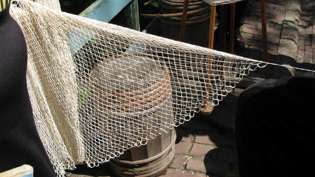 De mannen (in historisch kledij) repareren de visnetten. The men (in historical clothing) repair the fishing nets. Les hommes (en tenue historique) réparent les filets de pêche. Die Männer (in historischer Kleidung) reparieren die Fischernetze.