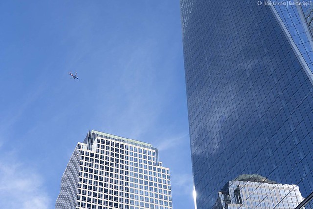 One World Trade Centerin lasiseinää, sinistä taivasta ja lentokone taivaalla