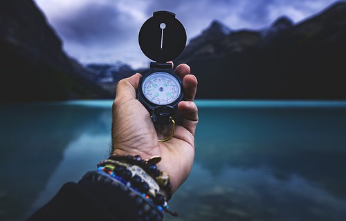 Hand holding compass in front of mountains and a lake. From Through the Eyes of an Educator: The Waiting Game – 5 minutes to forever