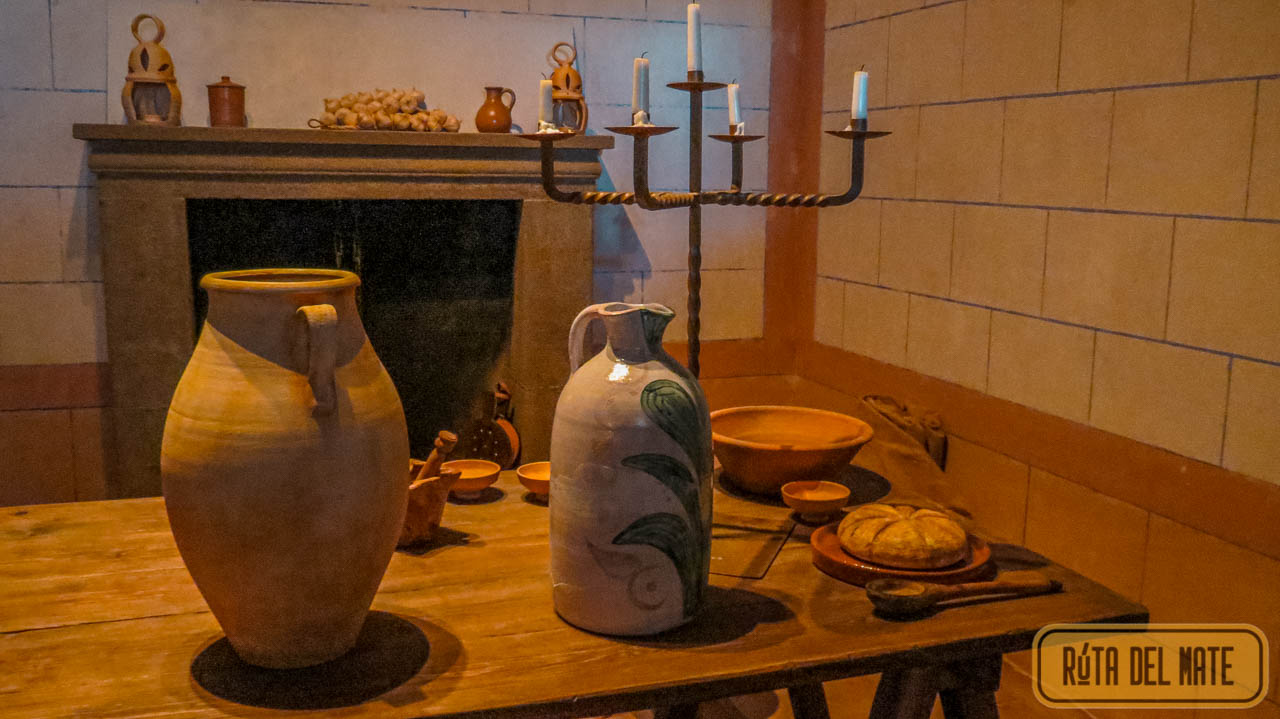 Kitchen of the Belmonte Castle. In the background there is a fireplace, in front a sturdy wooden table with several bowls and cooking utensils. 