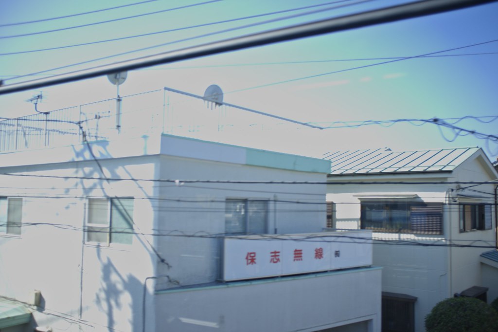 A blurry photo of two white buildings in Saitama, Japan, taken from the inside of a train travelling along an elevated track