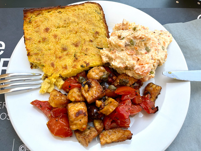 A photo of a white plate with three items on it: a yellow slice of something (corn related?), some Russian salad, and a mixture of red peppers and something that is like Tofu but was something else that I forget.