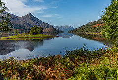 Reflections, headlands, woodland and a pyramidal peak called the Pap of Glencoe from near to the eastern end of Loch Leven, looking west, Highland Region, Scotland.