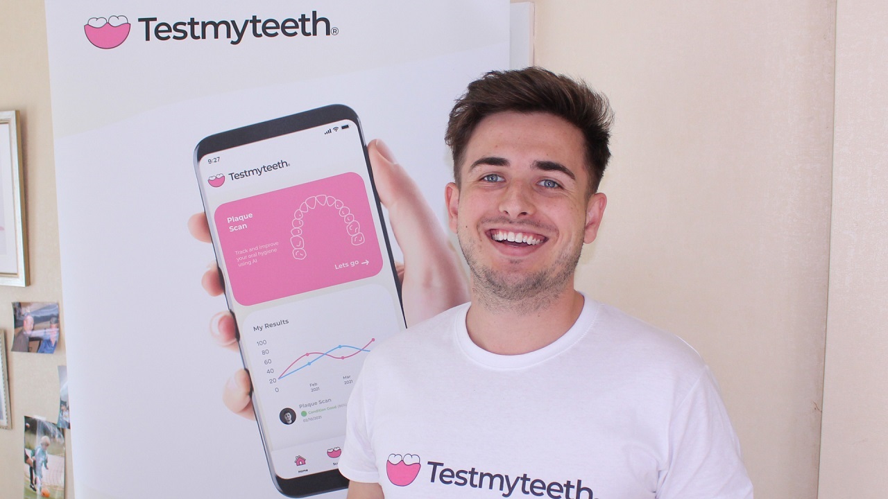 male student holding phone with testmyteeth app showing, standing in front of branded banner stand
