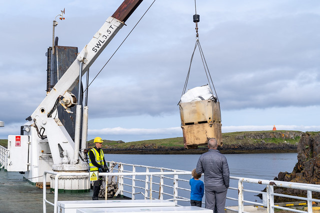 Stykkisholmur, Iceland - July 2, 2023: Employee loads cargo onto the Ferry Baldur in Iceland, as a father and son passengers watch