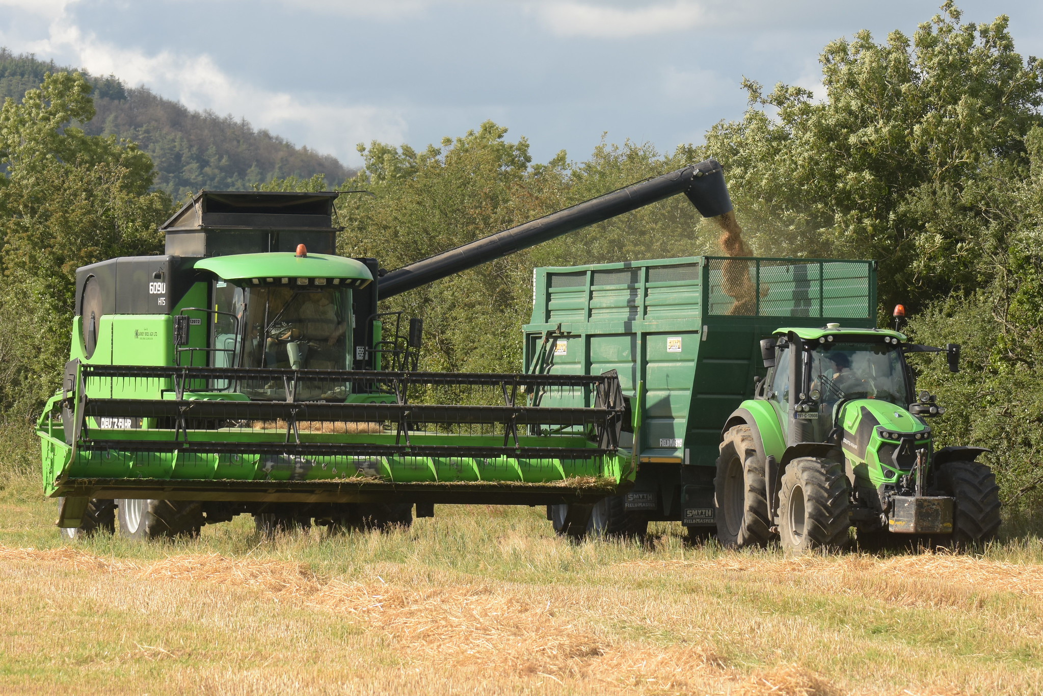 Deutz Fahr 6090 HTS Combine Harvester unloading Winter Barley to a Smyth Trailers Field Master Super Cube Trailer drawn by a Deutz Fahr Agrotron 6185 Tractor
