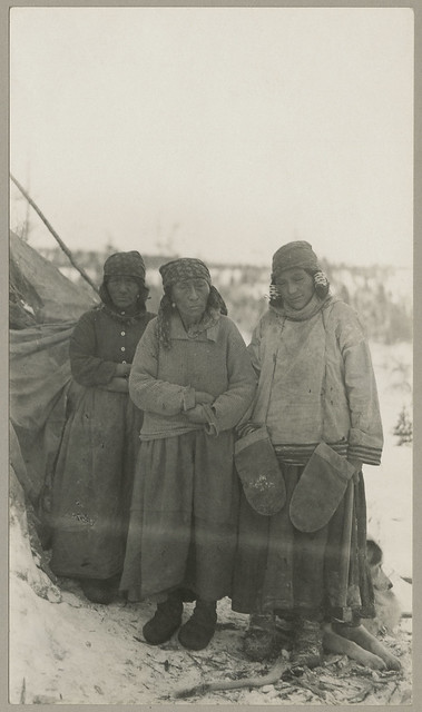 Three Innu women. The woman on the right is wearing hair ties and large mittens around her neck, Voisey's Bay, Newfoundland and Labrador / Trois femmes innues. Celle de droite porte des attaches à cheveux, et de larges moufles pendent à son cou, Voisey’s