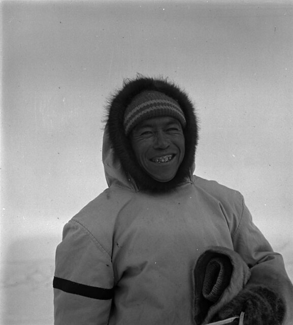 Inuk man smiling and wearing a white parka and fur mittens, Nunavut / Un Inuk souriant et portant un parka blanc et des moufles en fourrure, Nunavut