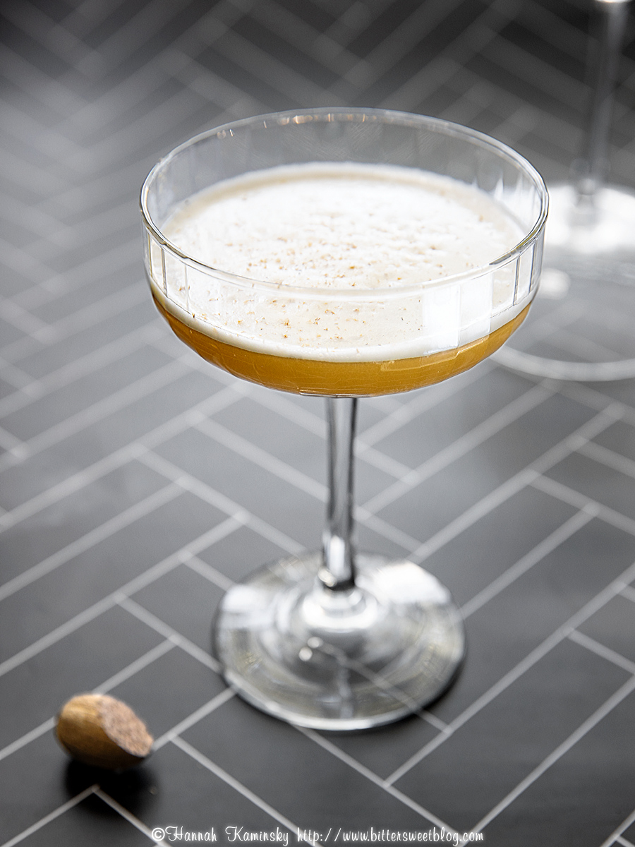 A coup glass of a frothy cocktail with nutmeg sprinkled on top.