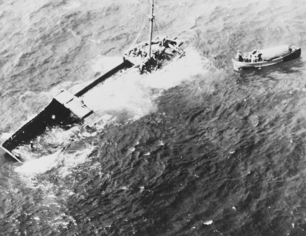 A Japanese Cargo Vessel Semi-submerged in the Western Pacific with six Japanese on board, February 1945. A US Navy whaleboat from the USS MAKASSAR STRAIT (CVE-91). is nearby.