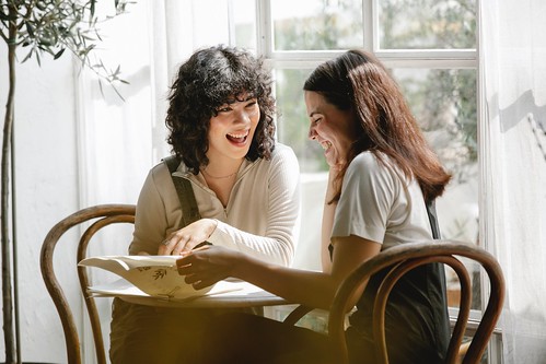 Two women sit at a table and smile. A stack of papers sits beneath them - Reading & Writing Skills Matter in Every Job