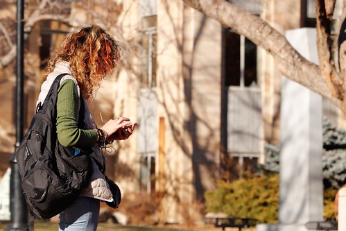 A woman wearing a black backpack stands outside and looks down at her phone - The Summer Before College Checklist  