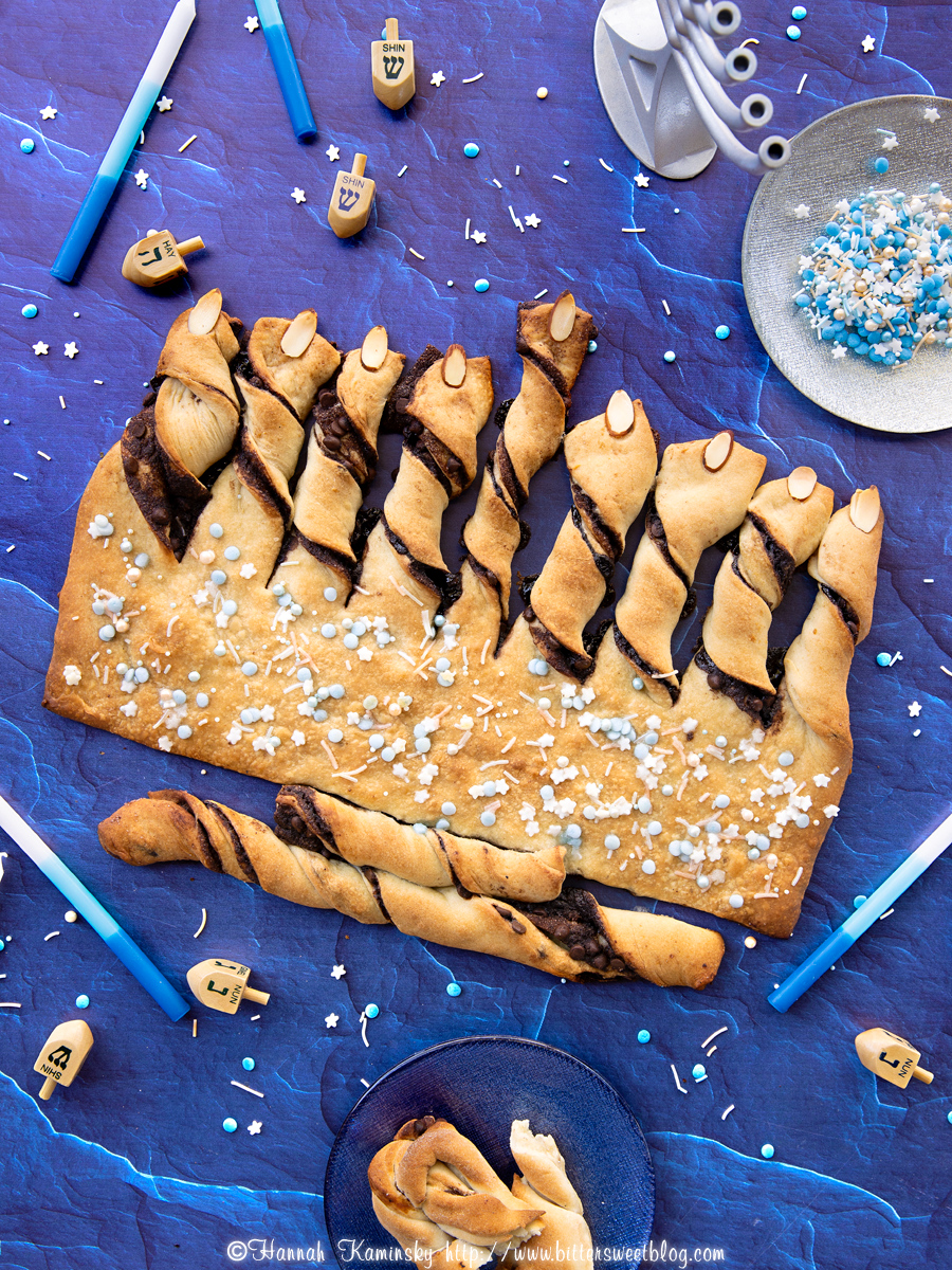 Babka bread fashioned into the shape of a menorah, surrounded by candles and dreidels. 