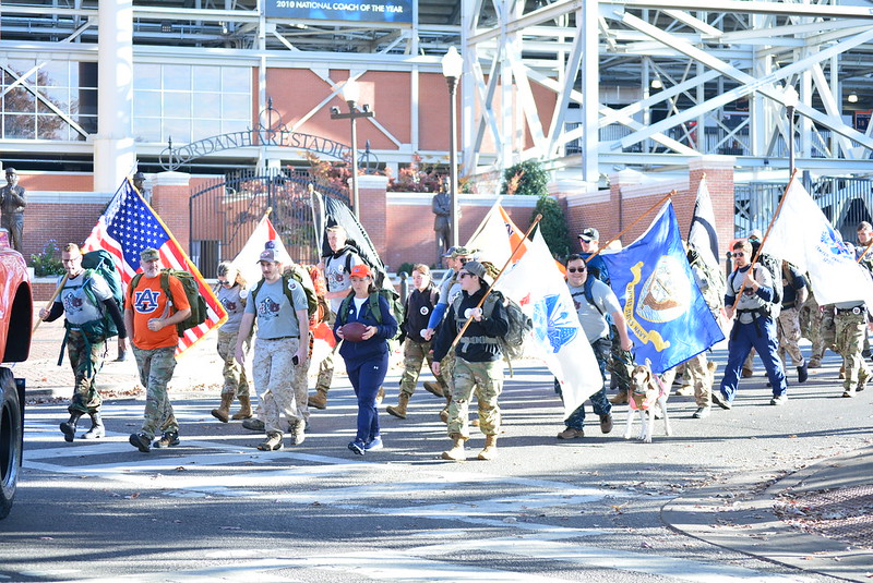 A group of people walk by Jordan-Hare Stadium carrying flags