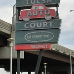 Tulsa Auto Court Tulsa Auto Court is one of several neon signs at Route 66 Neon Sign Park in Tulsa, OK.  When it lights up at night, there are green neon tubes above and below both Tulsa and Court.  All of the words and outline of the car are white tubes.

This park is located at the Southwestern end of the 11th Street Bridge.  This was historically the bridge which carried Route 66 over the Arkansas River near downtown Tulsa.  This bridge was bypassed and closed in 1980, but preserved for its Route 66 history.

The park contains three motel neon signs: Will Rogers Motor Court, Oil Capital Motel, Tulsa Auto Court.  Each of these were prominent motels along Route 66 in the Tulsa area.  Sadly, the original neon signs no longer exist, and these are replicas.  They do light up at night.  There is no parking here, so your best bet is to park in the lot a block east of Cyrus Avery Plaza, and walk across the replacement bridge here.

There is a marker about the motel, which reads:
Tulsa Auto Court
8833 East Admiral Place
When Route 66 was originally established in 1926, it came into Tulsa from the east on 11th Street but turned north on Mingo road for one mile and continues into town on Federal Drive (now Admiral Place).  Although the Tulsa Auto Court was established in the 1950s-long after highway 66 was re-aligned to take 11th Street all the way into downtown-it joined a host of other automobile-and-traveler related businesses that were established during those early Mother Road years.  The neon sign out front was a vibrant way to encourage people to stop for the night.  Originally owned and operated by Mrs. Charles Wyatt, this motel also featured wall furnaces, full tile bathrooms, and kitchenettes.  It continued to be known as the Tulsa Auto Court until 1989.