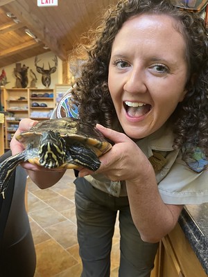 A Ranger poses with a turtle in a Visitor Center. 