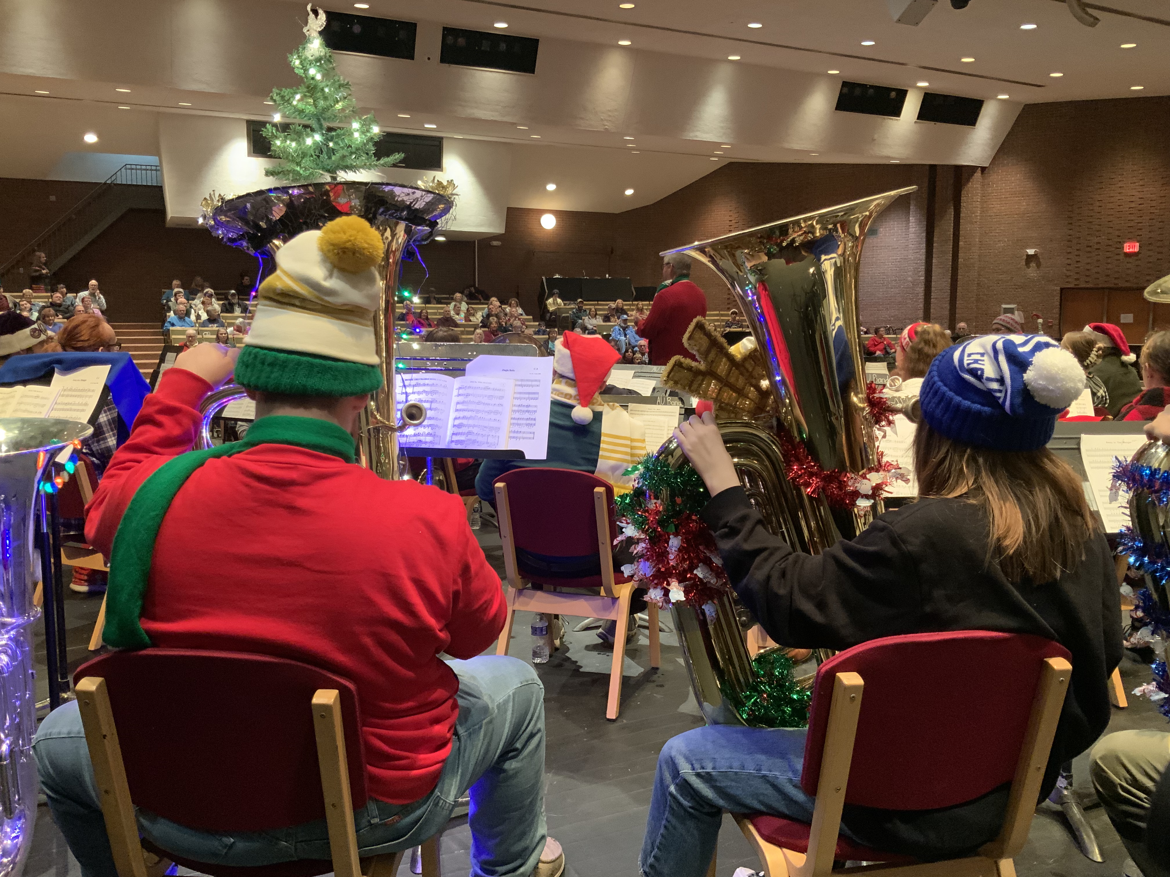 Members of the 2023 Ashland TubaChristmas ensemble and audience. One of the tubas has Christmas lights and even a lit up Christmas tree on its bell.